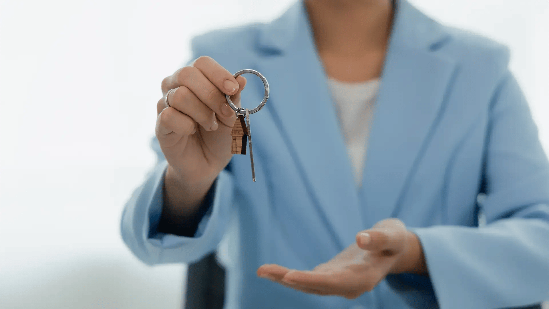 Persona con traje azul sosteniendo una llave con llavero de casa, representando un proceso de juicio de arriendo.