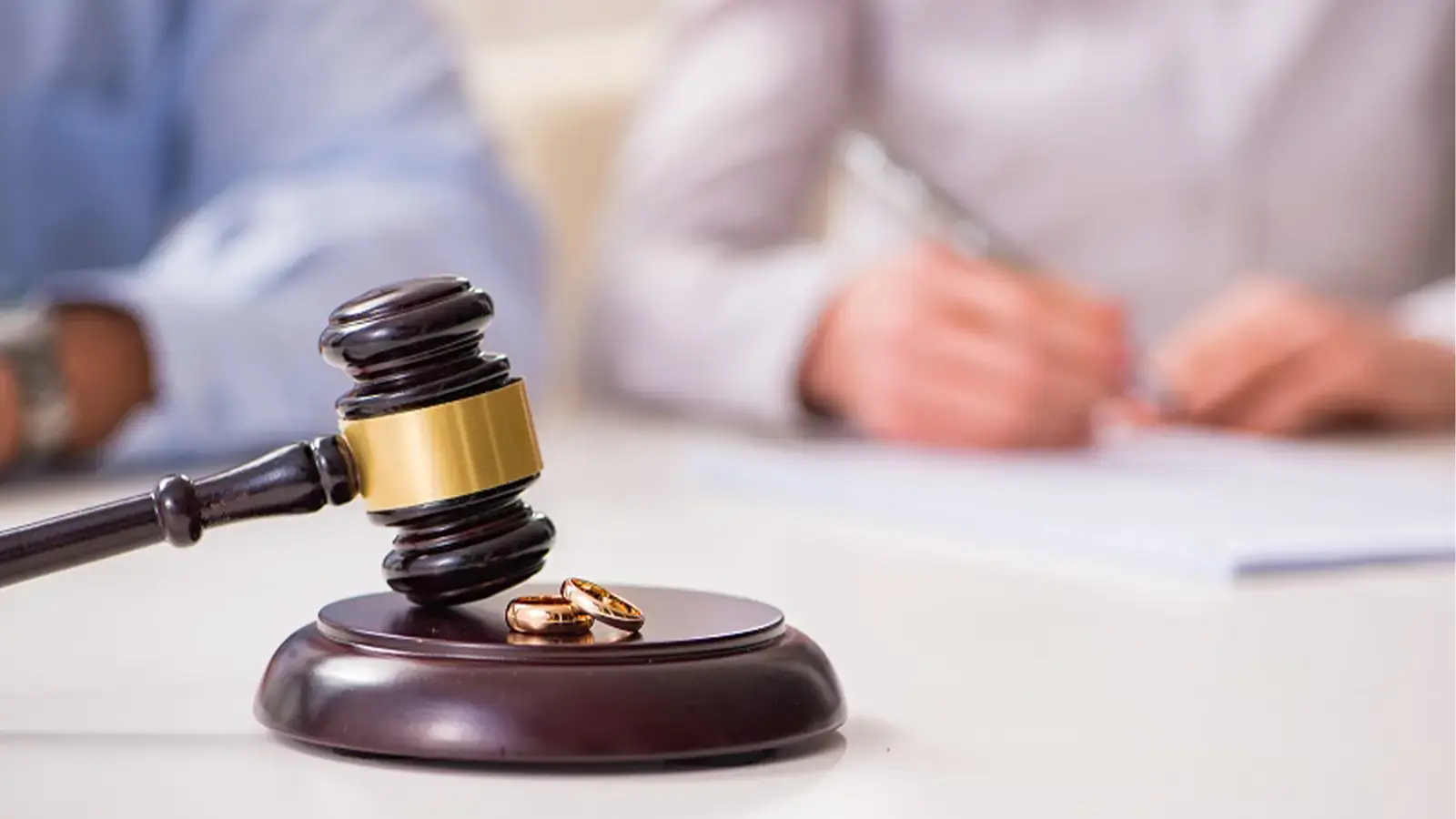 Divorcio. Pareja firmando divorcio frente a mazo de juez y sus dos anillos