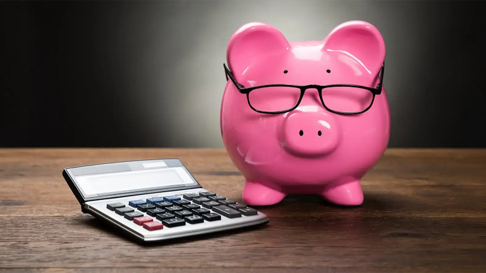 Tips financieros. Alcancía de cerdito rosado con lentes y una calculadora